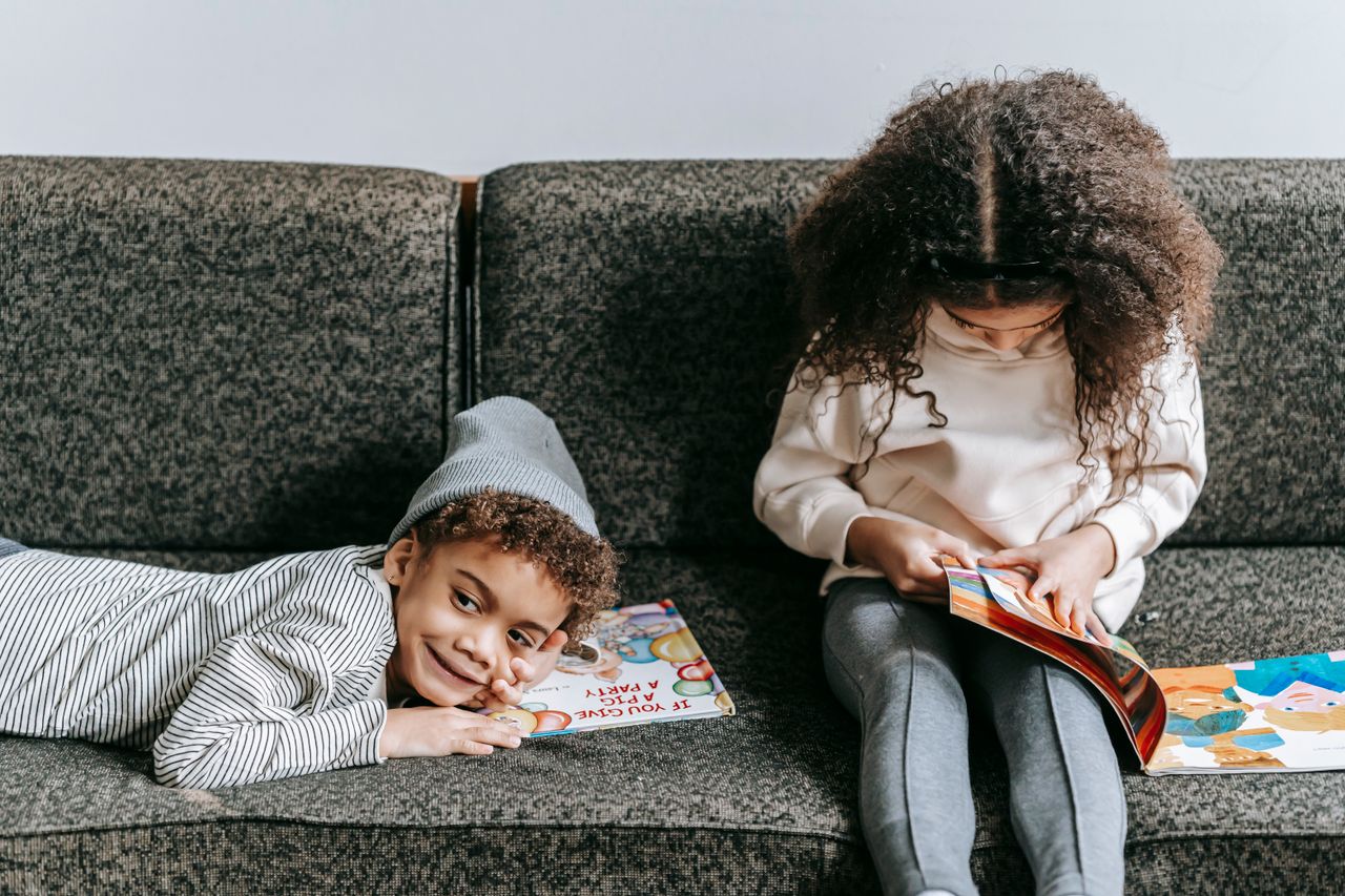 Adorable positive African American children resting on comfy couch with books in light living room