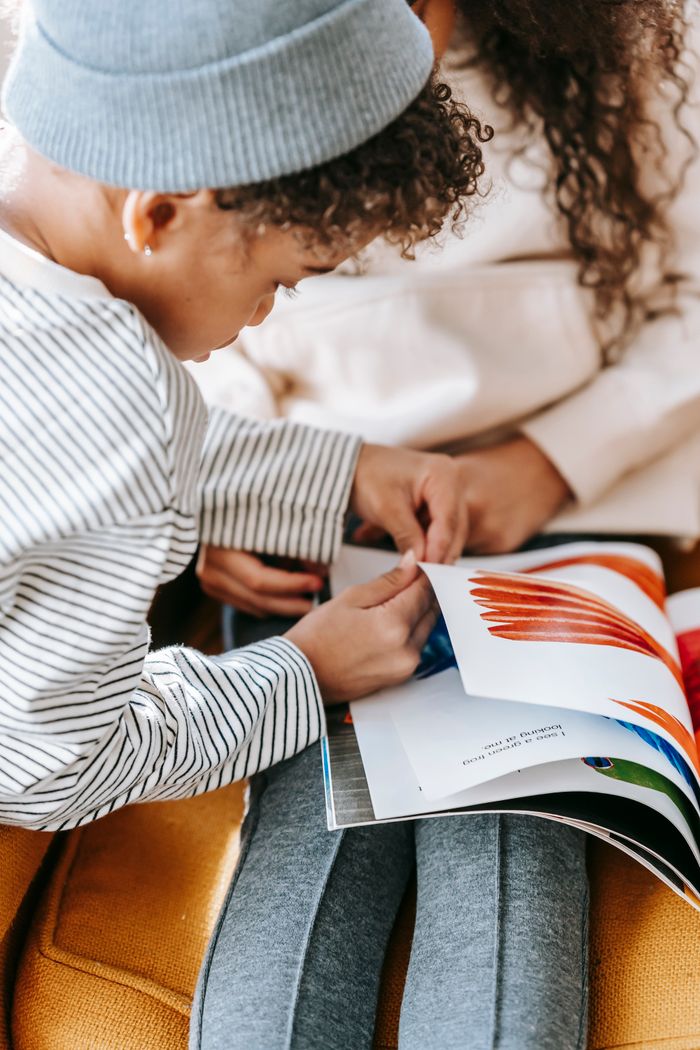 From above of crop anonymous African American little girl and boy reading book together while sitting on sofa
